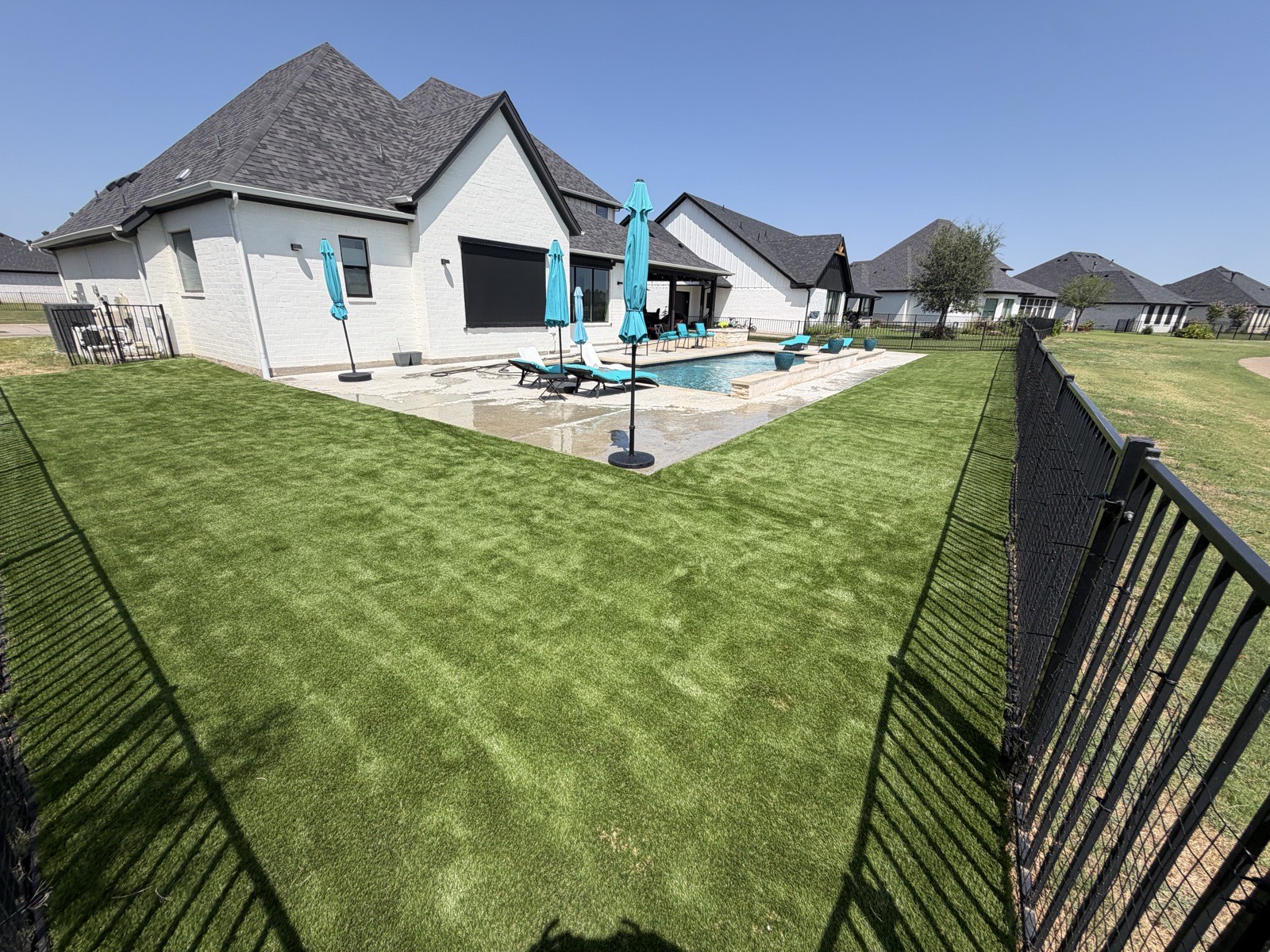 Artificial turf lawn wrapping around a backyard pool and patio