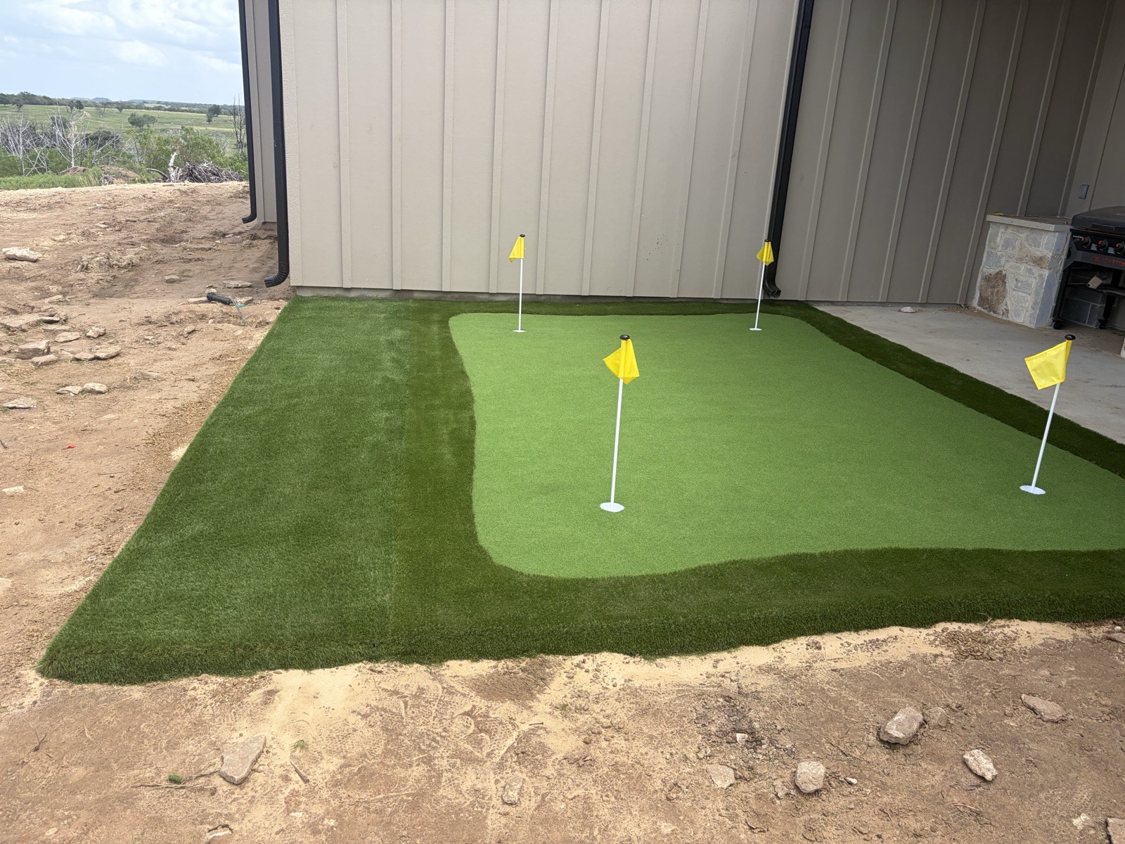 Large artificial turf lawn behind a house with an in-ground trampoline